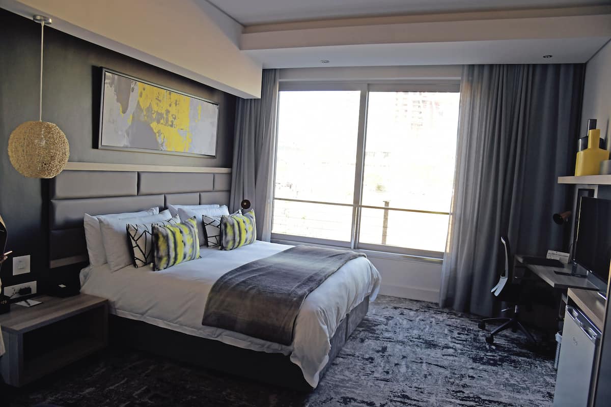A modern hotel room with a large bed, a desk, a chair, a television, and a window with curtains.