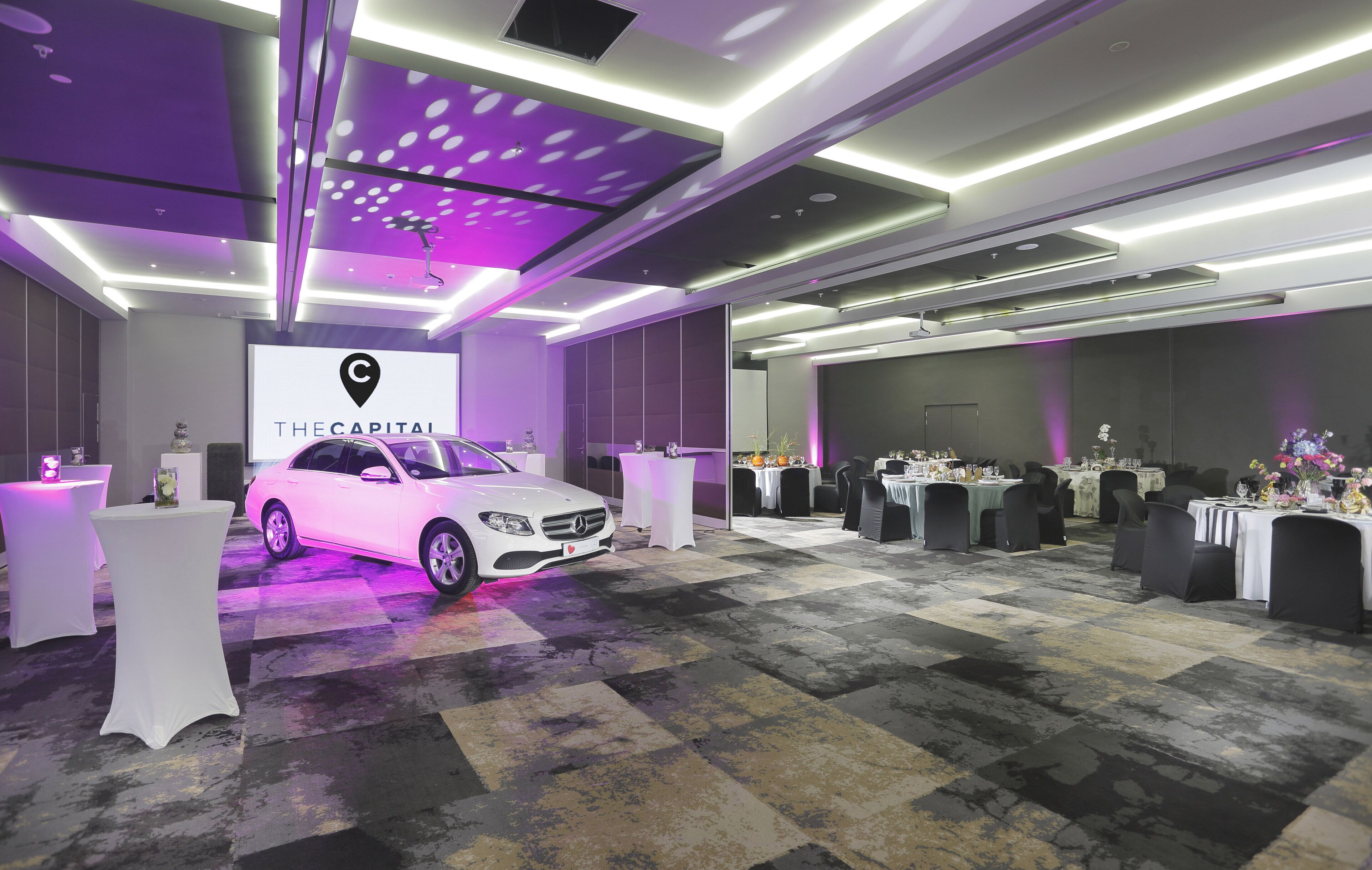 A modern hotel lobby with a white car, purple lighting, and a reception desk.