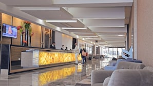 A modern hotel lobby with a reception desk, seating area, and large windows.