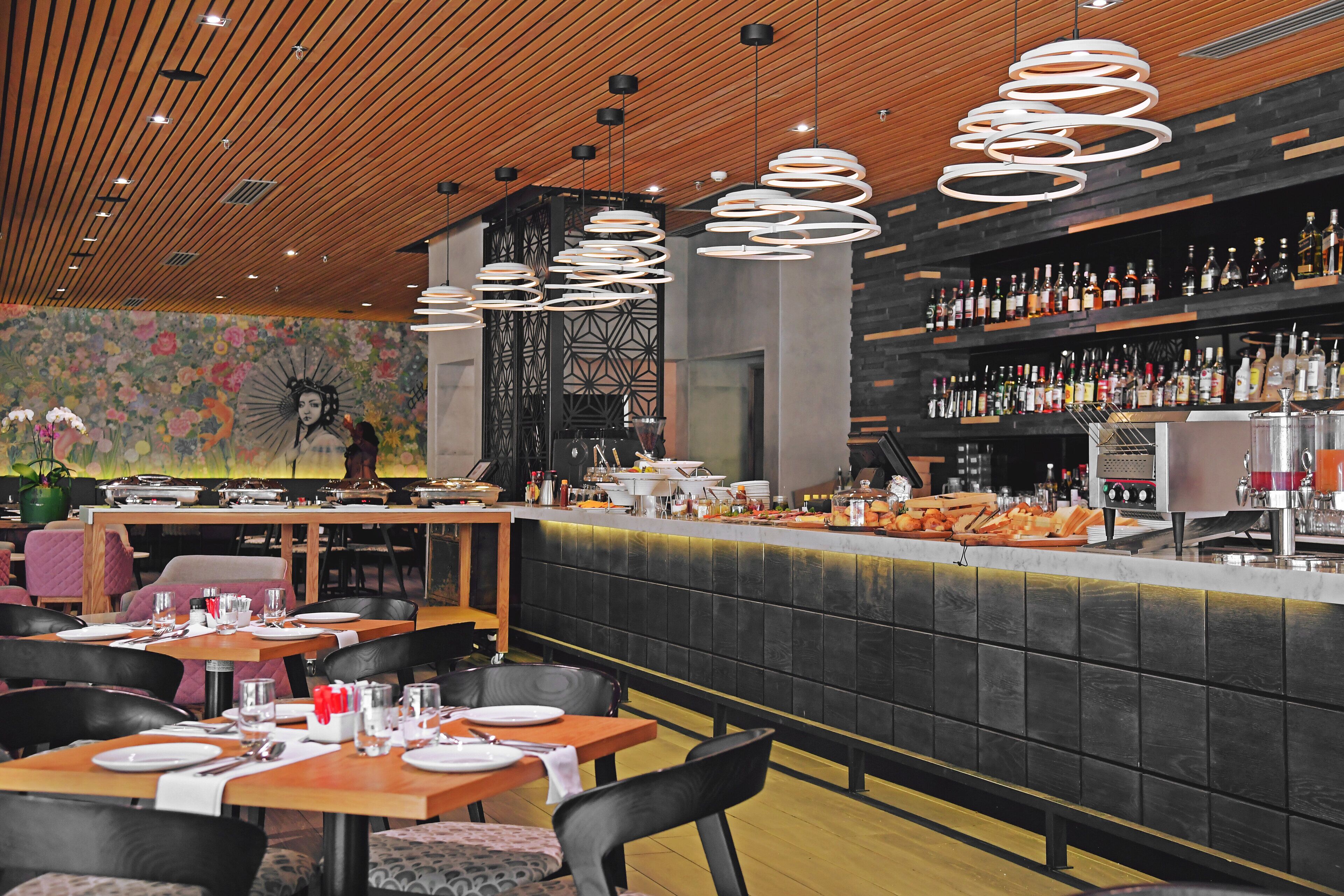 A restaurant with a bar area, wooden ceiling, and a floral mural on the wall.
