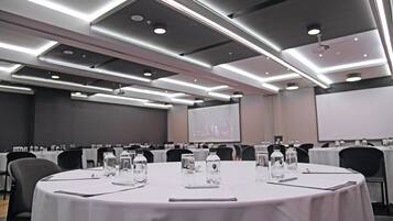 Un salón de conferencias con mesas redondas, botellas de agua y una pantalla de proyector.