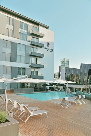 Un hotel con zona de piscina, tumbonas y sombrillas.