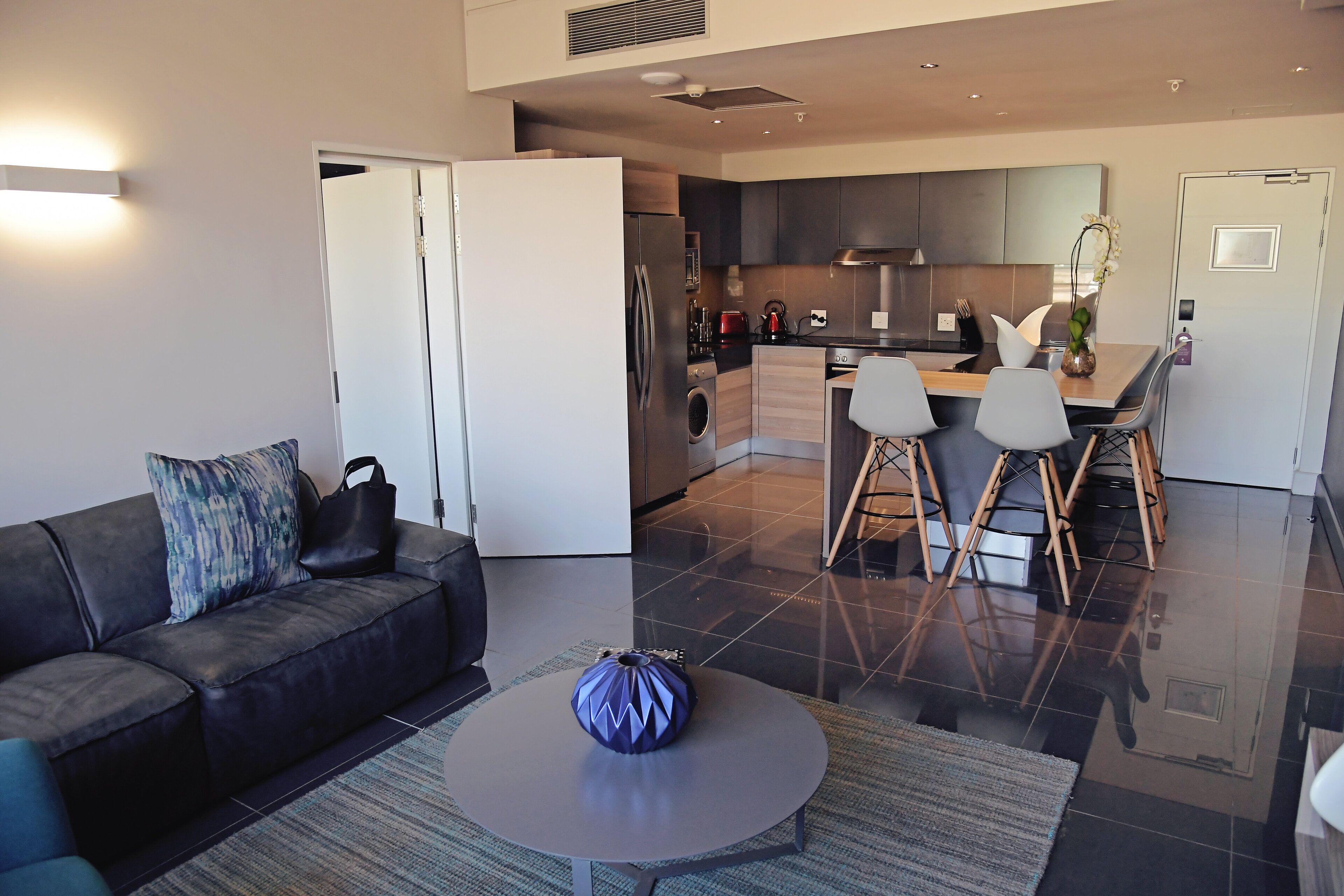 A modern living room with a sofa, a coffee table, and a kitchen area with a dining table and chairs.