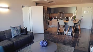 A modern living room with a sofa, a coffee table, and a kitchen area with a dining table and chairs.