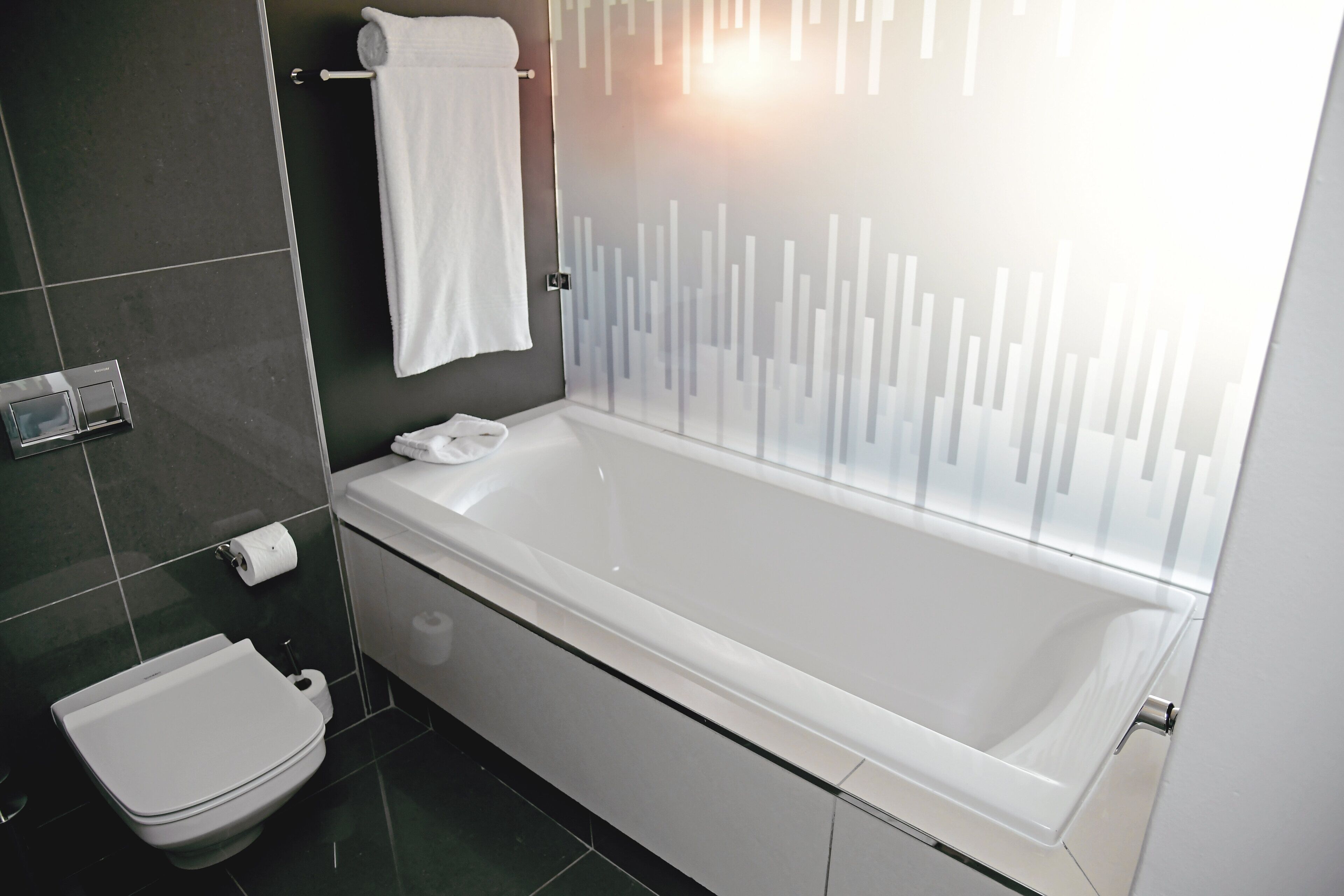 A modern bathroom with a white bathtub, a toilet, and a glass shower enclosure.