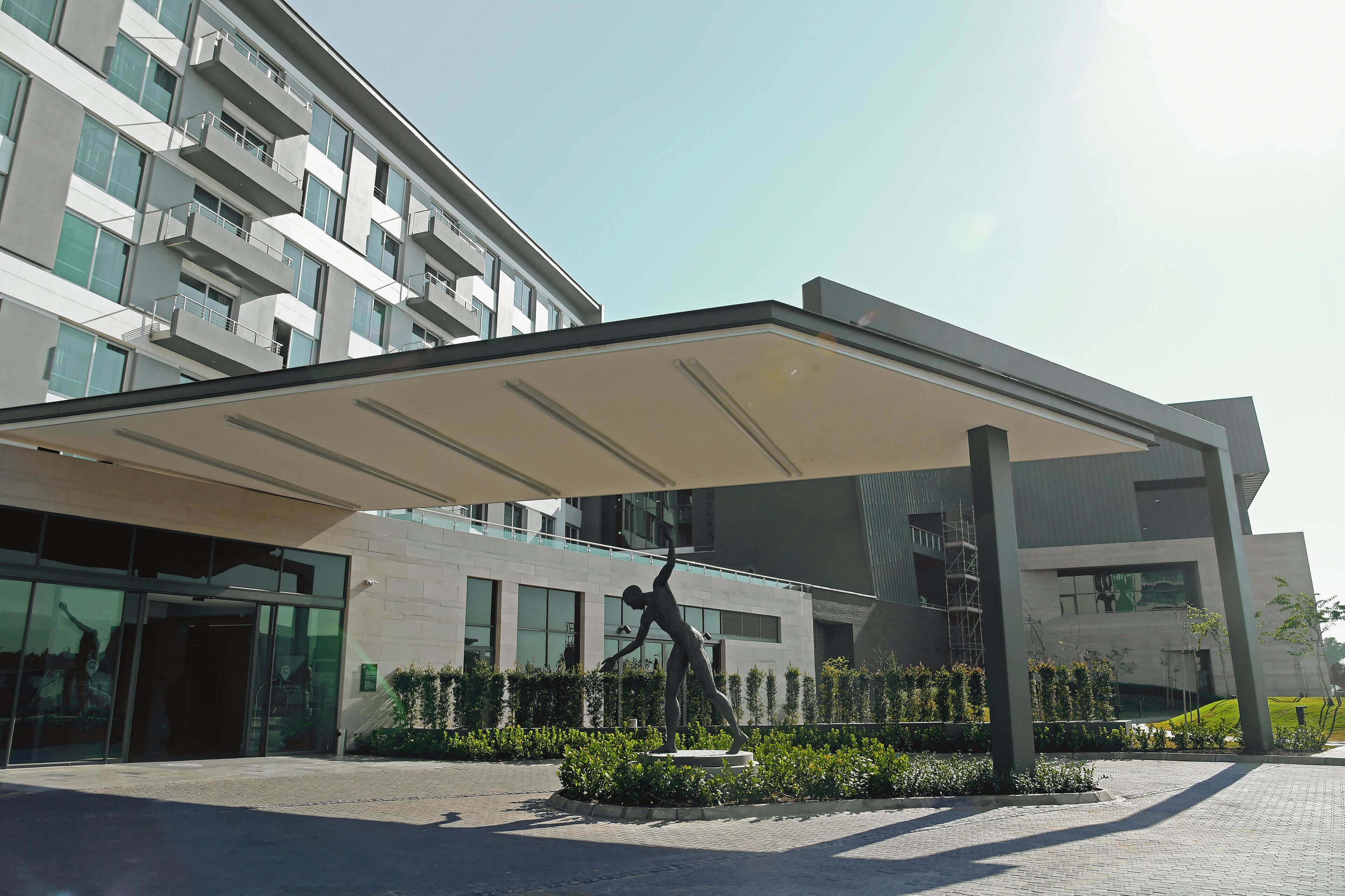 Um edifício moderno com entrada coberta, uma estátua e um jardim ajardinado.