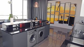 A modern kitchen with a built-in washer and dryer, a coffee maker, and a kettle on the counter.