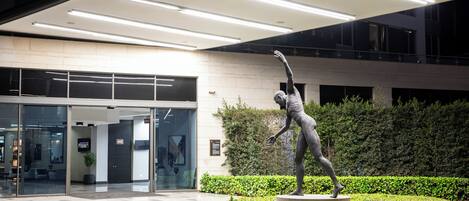 A modern building entrance with a statue of a figure in motion, surrounded by well-maintained greenery.