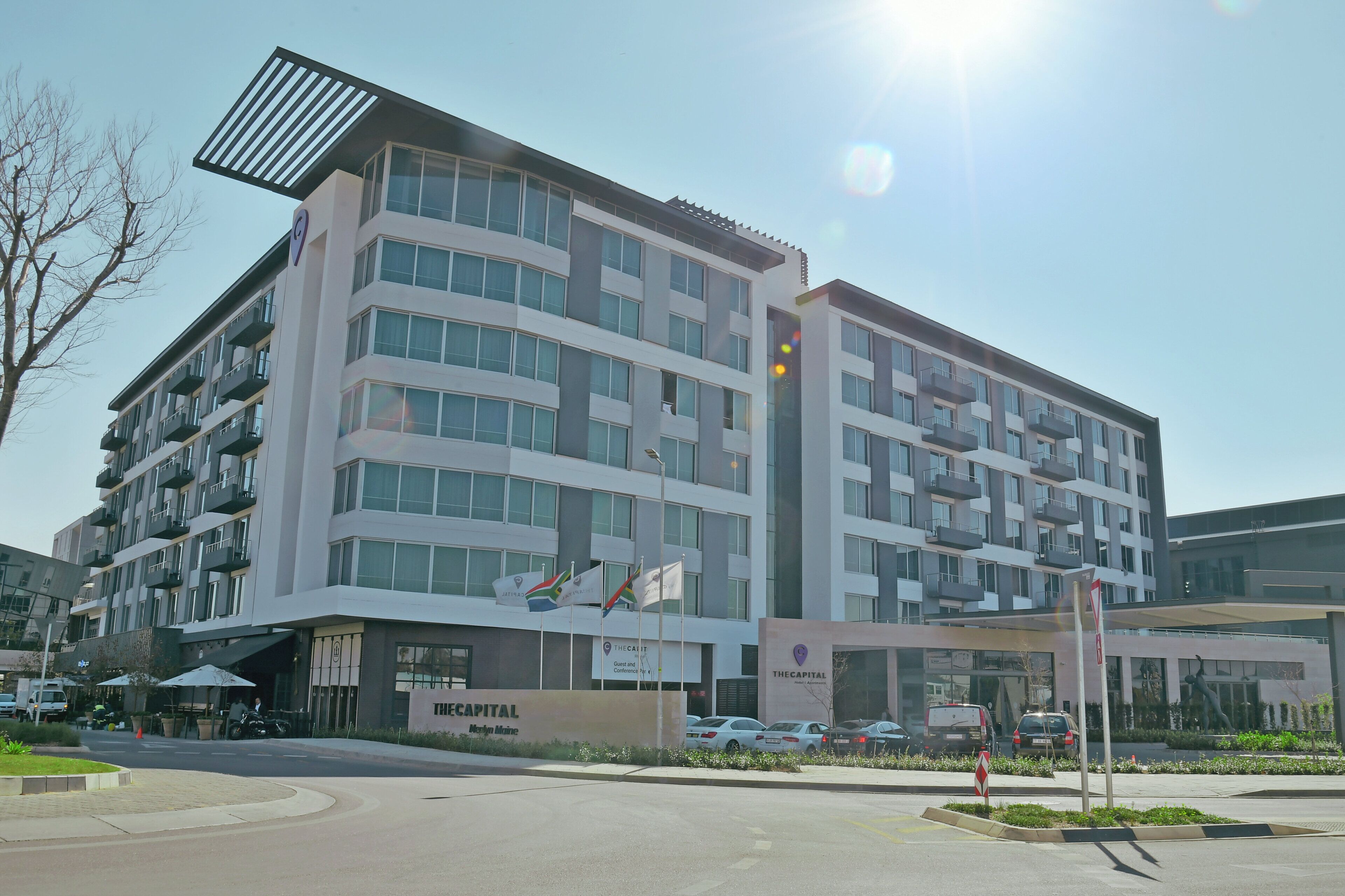 A multi-story hotel with balconies, a parking area, and flags.