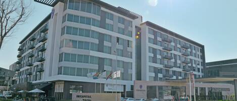 A multi-story hotel with balconies, a parking area, and flags.