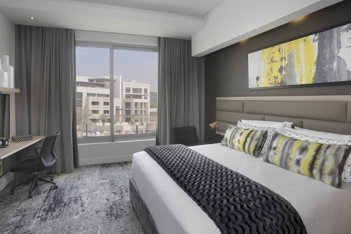 Habitación de hotel moderna con una cama grande, un escritorio y vistas a edificios a través del ventanal.