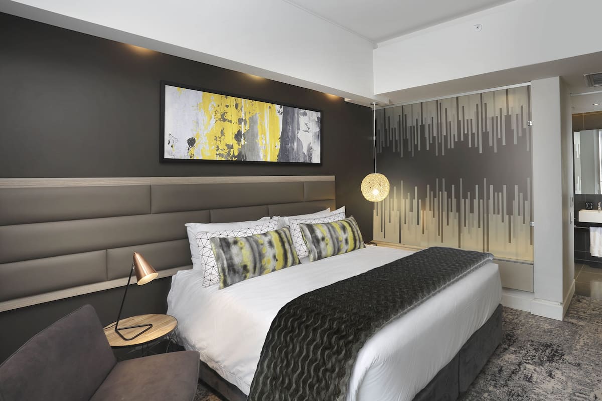 A modern bedroom with a large bed, a bedside table, a lamp, and a painting on the wall.