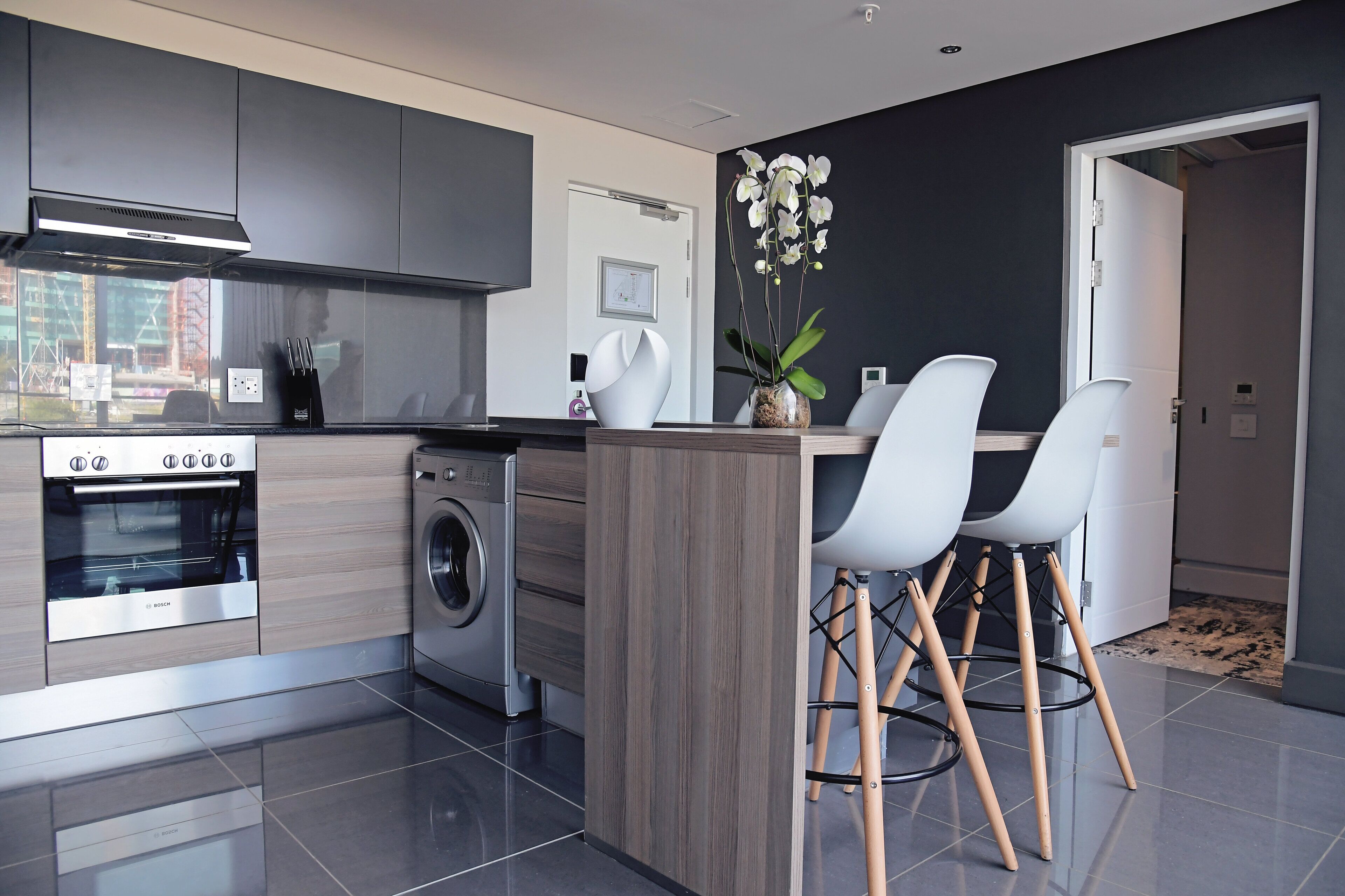 A modern kitchen with a built-in oven, washing machine, and a central island with bar stools.