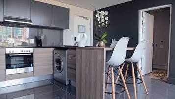 A modern kitchen with a built-in oven, washing machine, and a central island with bar stools.