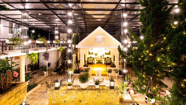 A spacious indoor area with a central seating area, multiple tables, and potted plants. - Le Petit Paris Hotel Dalat (Cam Ly - Da Lat)