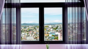 A room with a large window offering a city view, two wooden chairs, a small table, and a vase with flowers. - Le Petit Paris Hotel Dalat (Cam Ly - Da Lat)