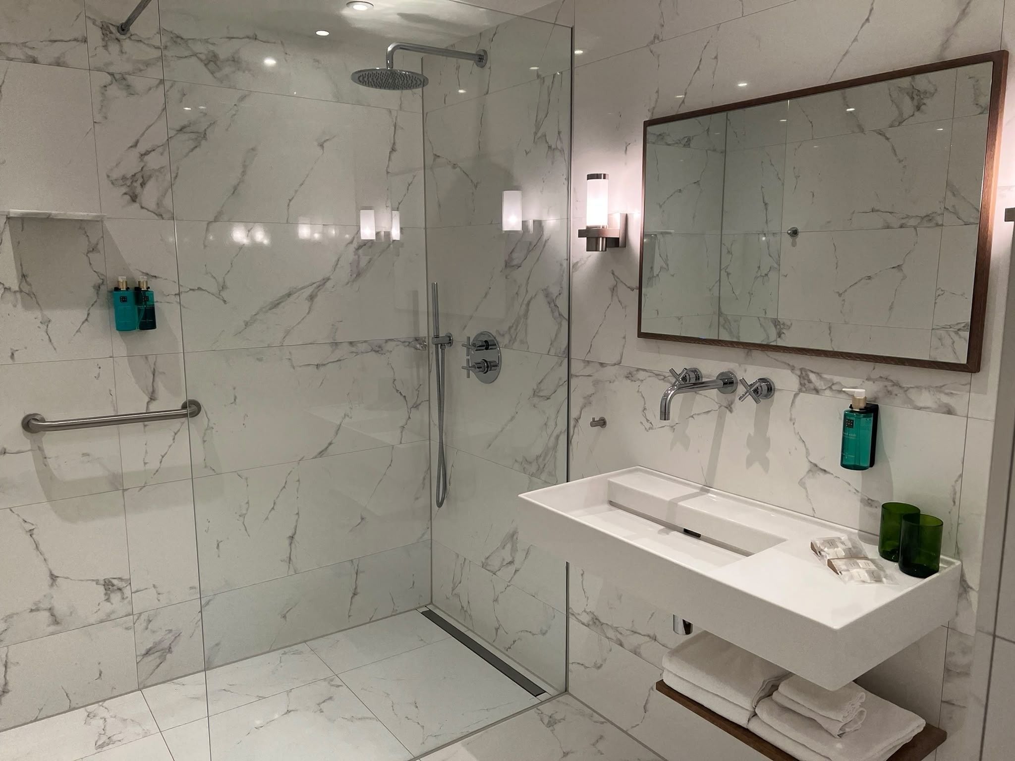 Un baño moderno con ducha envuelta en vidrio, un lavamanos blanco y un espejo grande.
