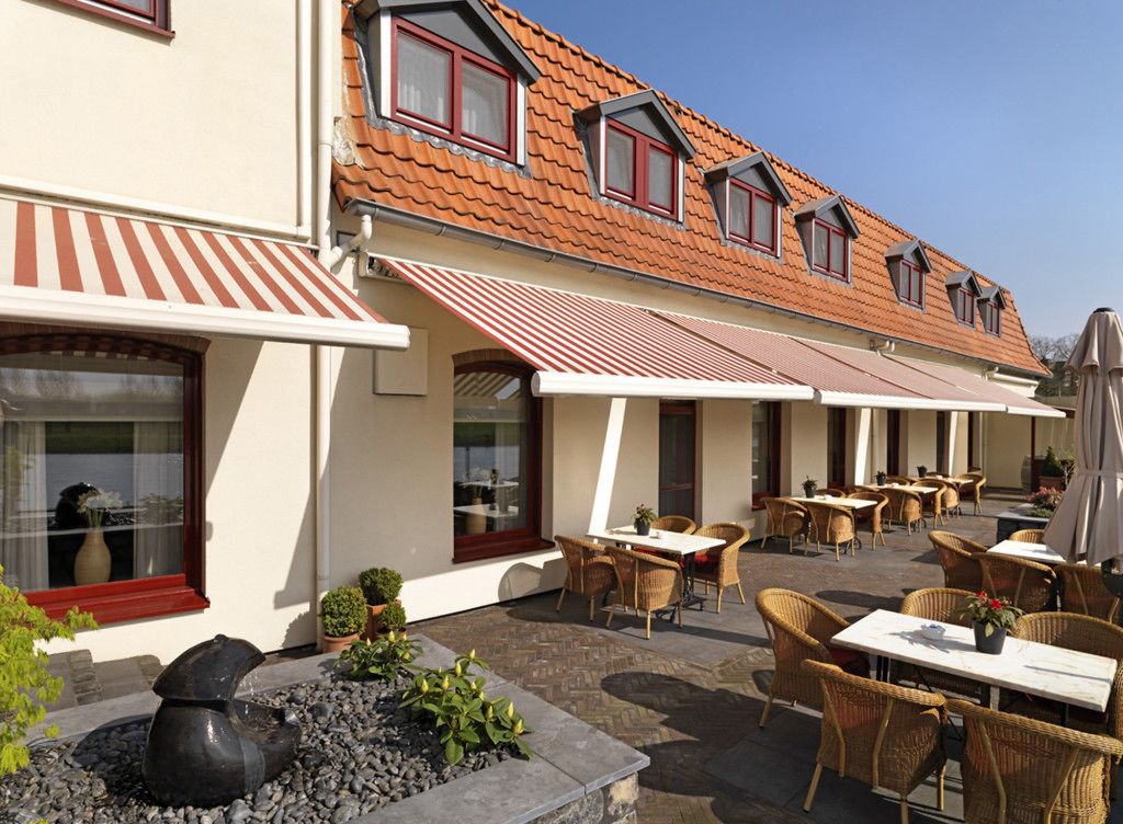 A building with a tiled roof, outdoor seating area with wicker chairs and tables, and a small garden with a water feature.