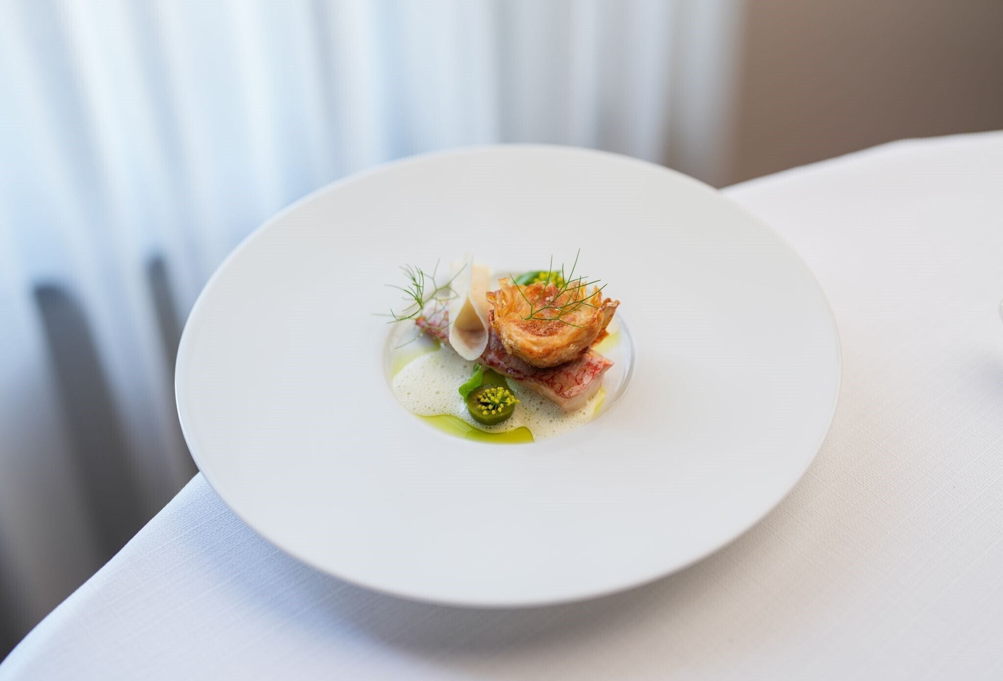 A white plate with a seafood dish, including fish and possibly crab, garnished with herbs.