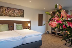 A hotel room with a bed, bedside lamps, a nightstand, a wall-mounted shelf, and a large floral painting. - Hotel Restaurant Valuas (Venlo)