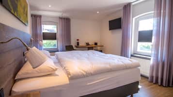 A modern hotel room with a large bed, a bedside table, a desk, and a TV.