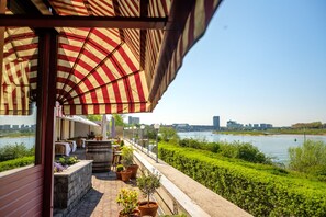 Terras met een gestreept zonnescherm, uitzicht op een rivier, plantenbakken en een panorama van de stadshemel.