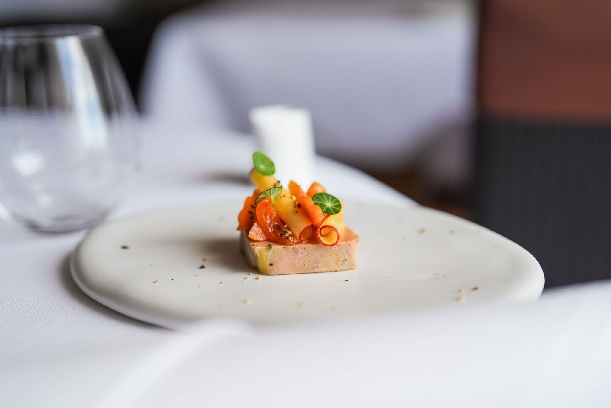 Un plato blanco con un pequeño alimento sobre un mantel blanco.