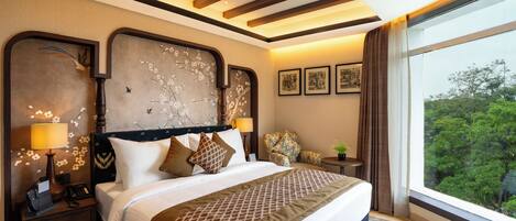 A hotel room with a large bed, nightstands, a desk, and a window with a view of trees.