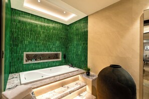 A modern bathroom with a large bathtub, green mosaic tiles, a marble countertop, and a large black vase. - Fortune Park Sishmo, Bhubaneswar - Member ITC Hotels' Group (Bhubaneshwar)