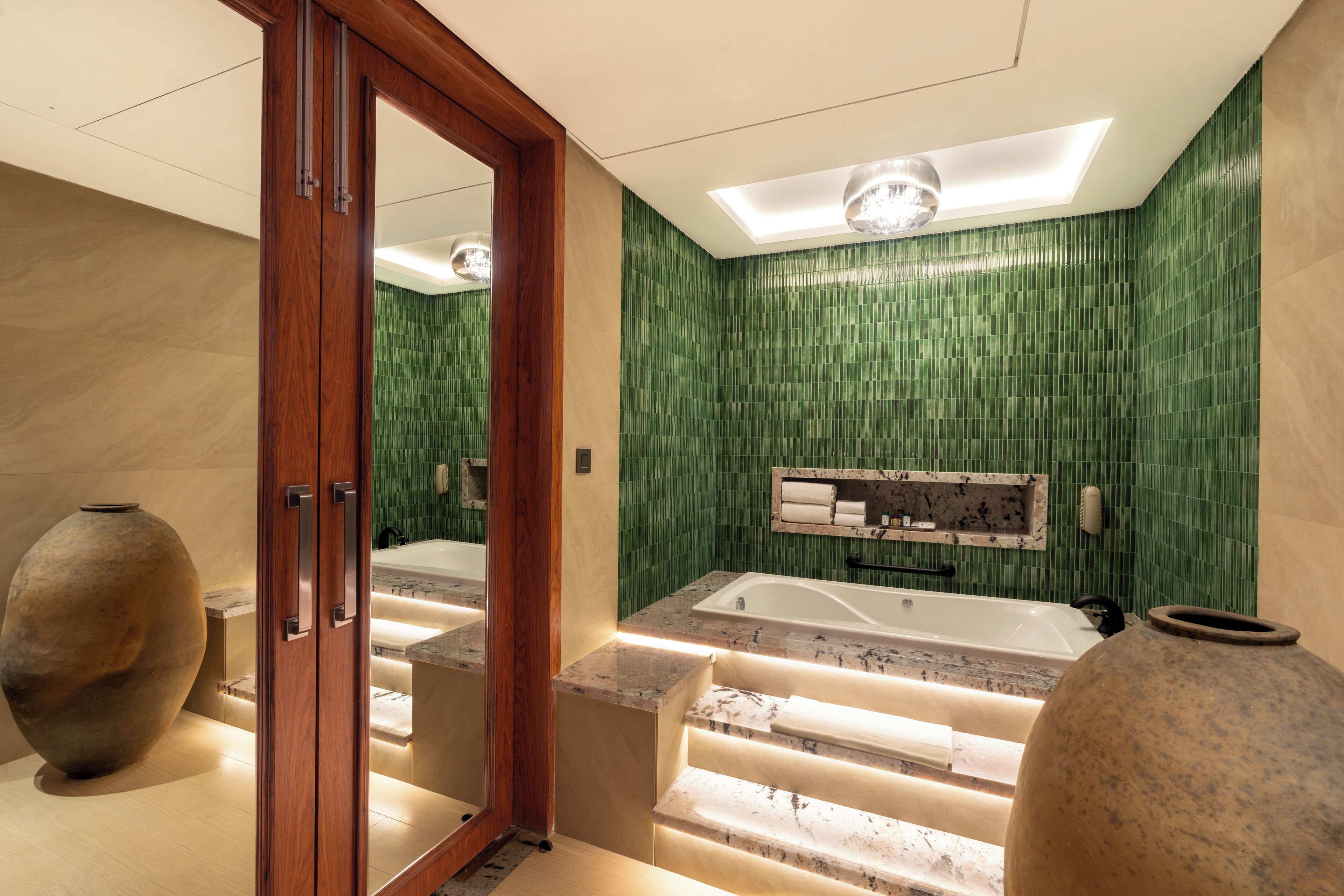 A modern bathroom with a large bathtub, a wooden door, and a green tiled wall.
