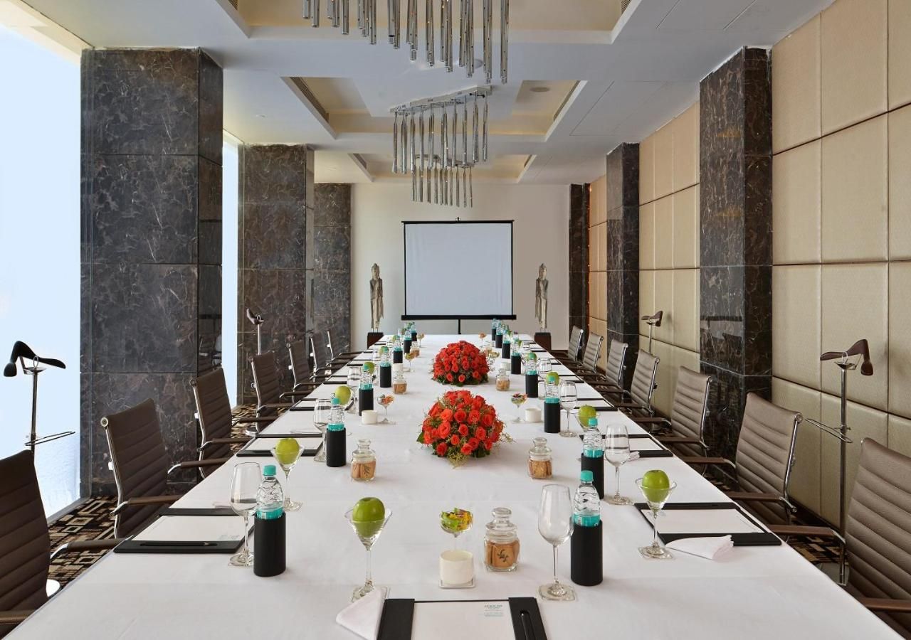 Un salón de conferencias con una larga mesa, sillas y una pantalla de proyector.