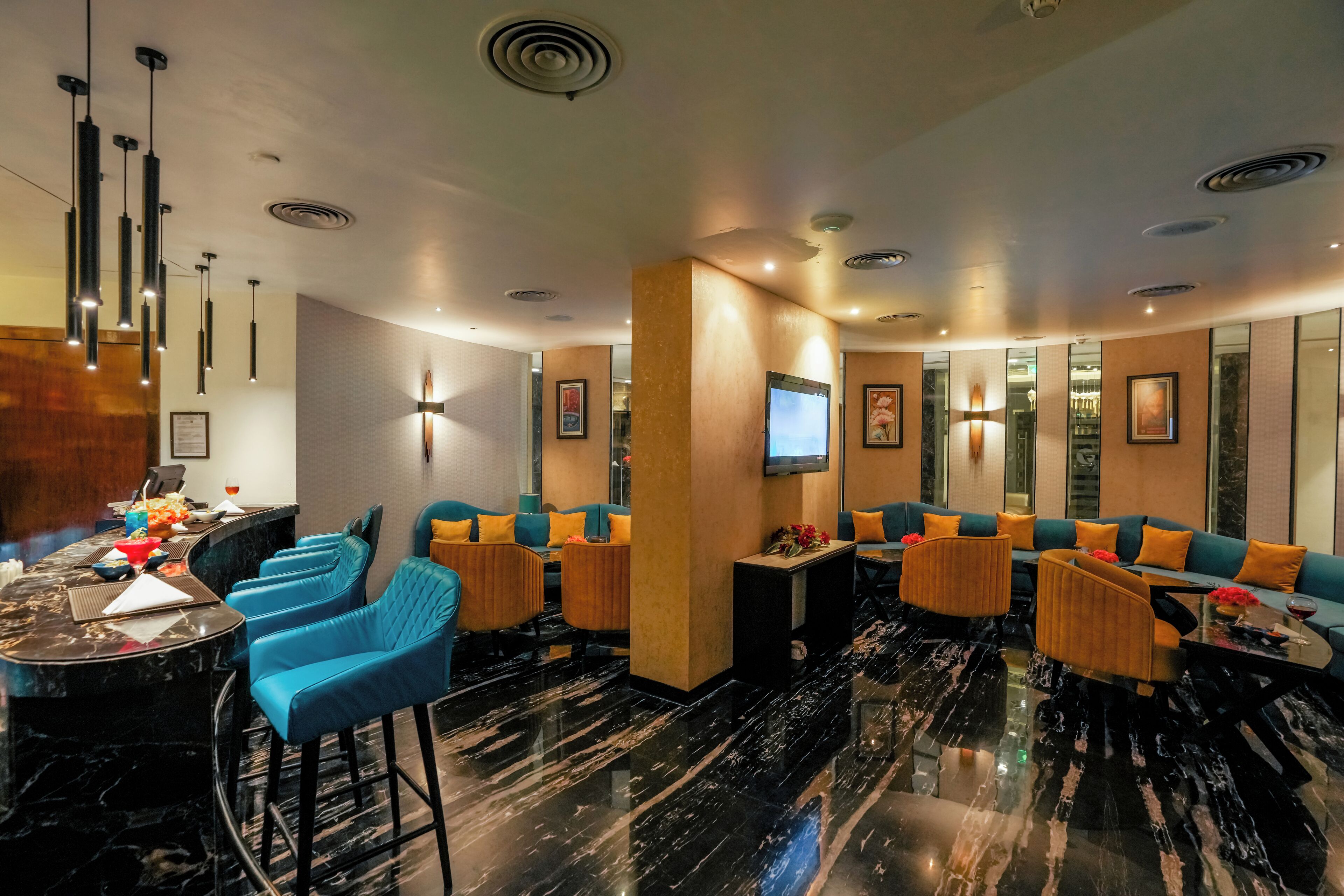 A modern hotel lobby with a marble floor, blue and orange seating, a bar area, and a television mounted on the wall.