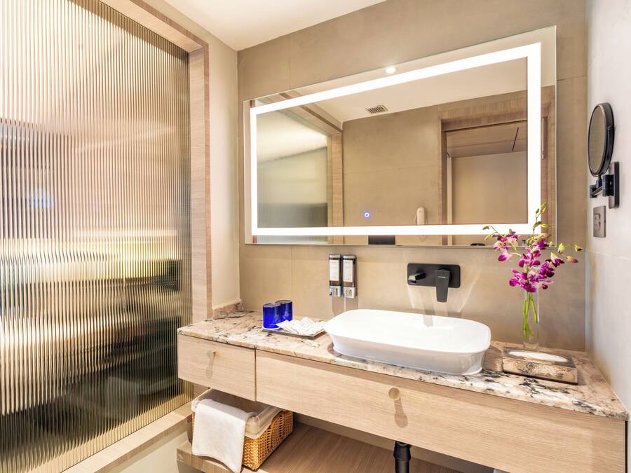 Een moderne badkamer met een grote spiegel, een witte wastafel en een vaas met bloemen.