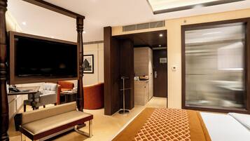 A hotel room with a bed, a sofa, a desk with a chair, a television, and a wardrobe.