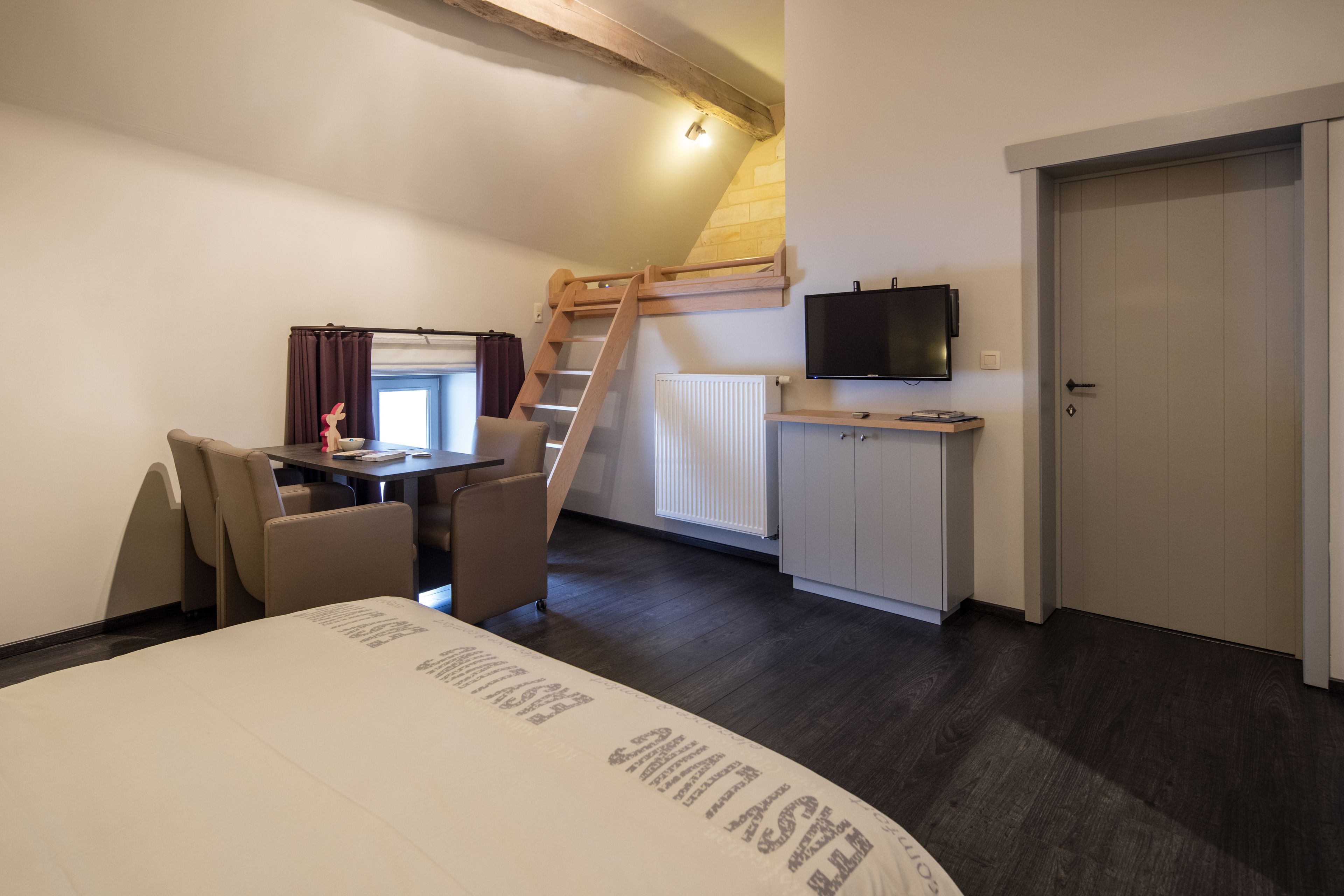 A bedroom with a bed, a desk, a chair, a TV, a door, and a staircase.
