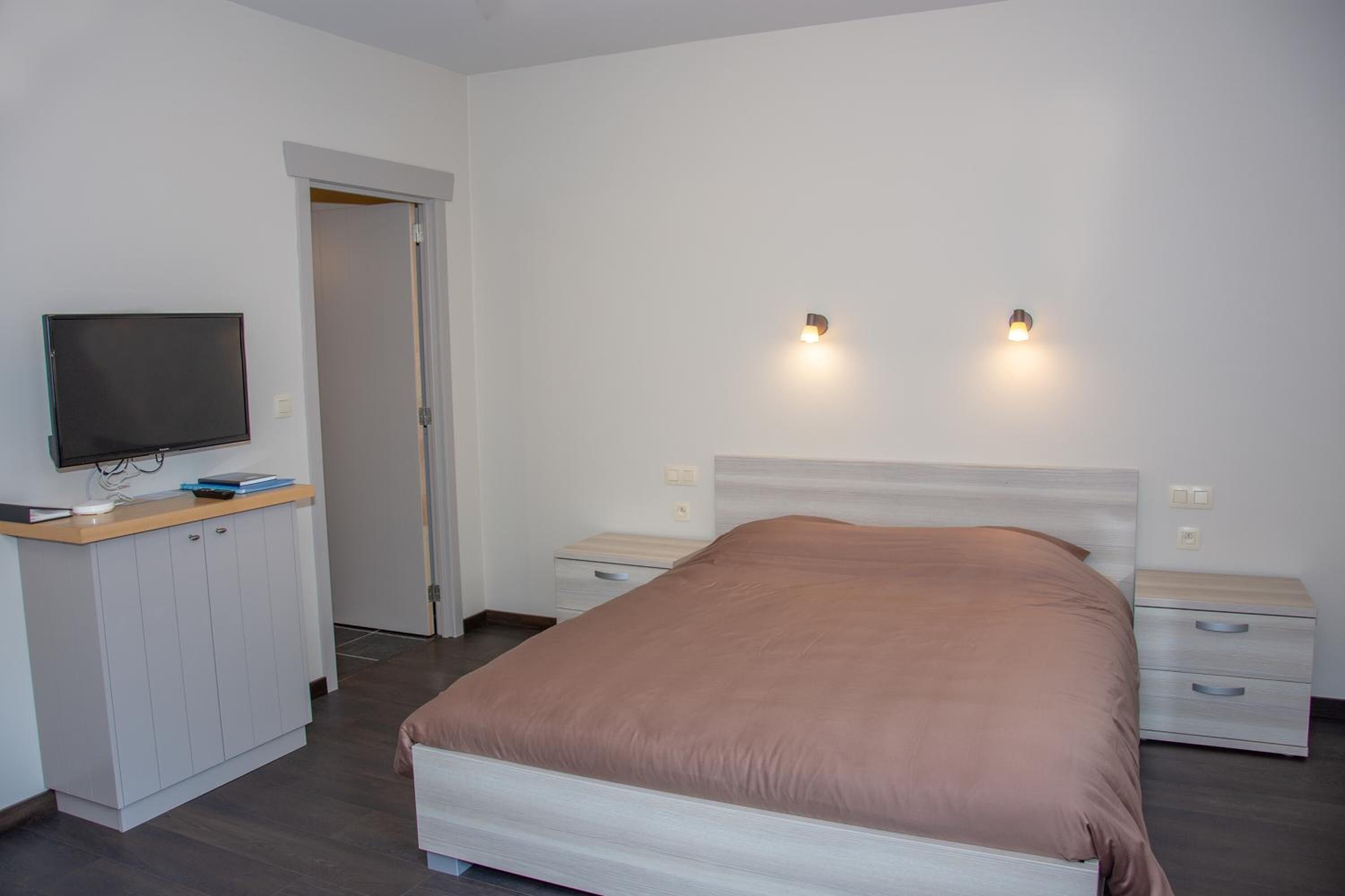 Quarto com cama, televisão sobre um aparador e duas luminárias de cabeceira.