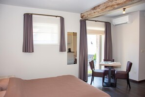 A hotel room with a bed, a dining table with chairs, a window with curtains, an air conditioning unit, and a view of the outside. - B&B de Oude Winning (Riemst)