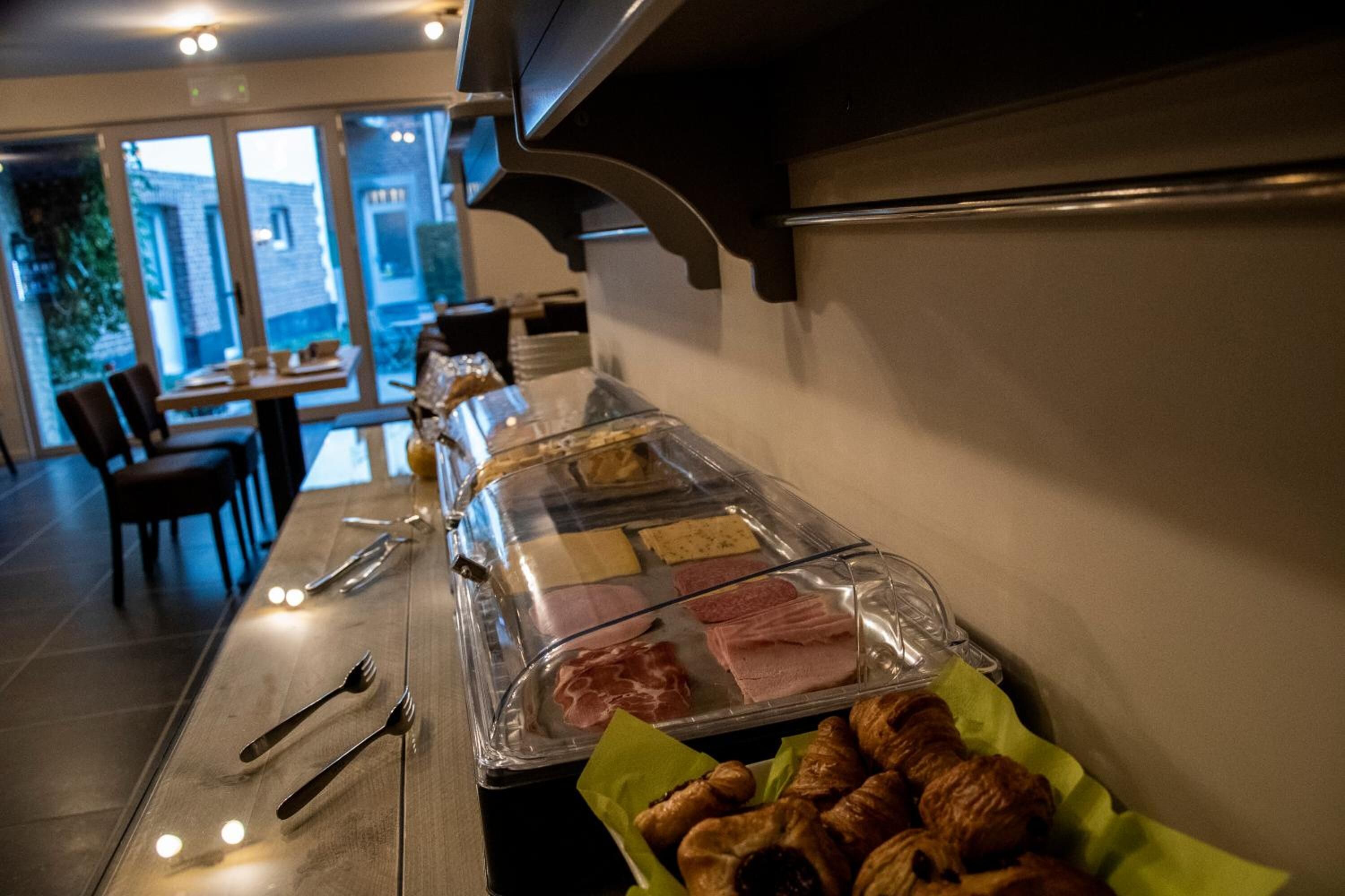 Un buffet proposant une variété de viandes et de pâtisseries, un espace repas avec des chaises et des tables, et une vue sur l’extérieur grâce à de grandes fenêtres.