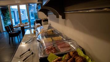 Un buffet proposant une variété de viandes et de pâtisseries, un espace repas avec des chaises et des tables, et une vue sur l’extérieur grâce à de grandes fenêtres.