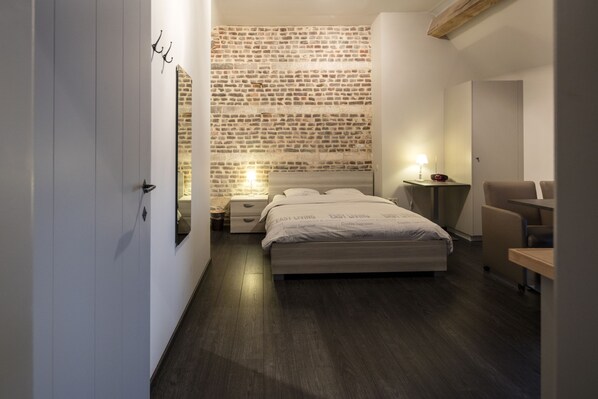 Ein modernes Schlafzimmer mit einem Kopfstück im Ziegelstein-Design, einem ordentlich bezogenen Bett, einem Nachttisch mit Lampe und einem Sessel.