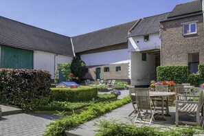 Ein Innenhof mit Außenbestuhlung, einer Hecke und einem kleinen Gebäude mit blauem Dach.