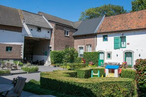 Ein Innenhof mit einem Backsteinhaus, einem weißen Gebäude mit grünen Fensterläden und einem kleinen Spielhäuschen.