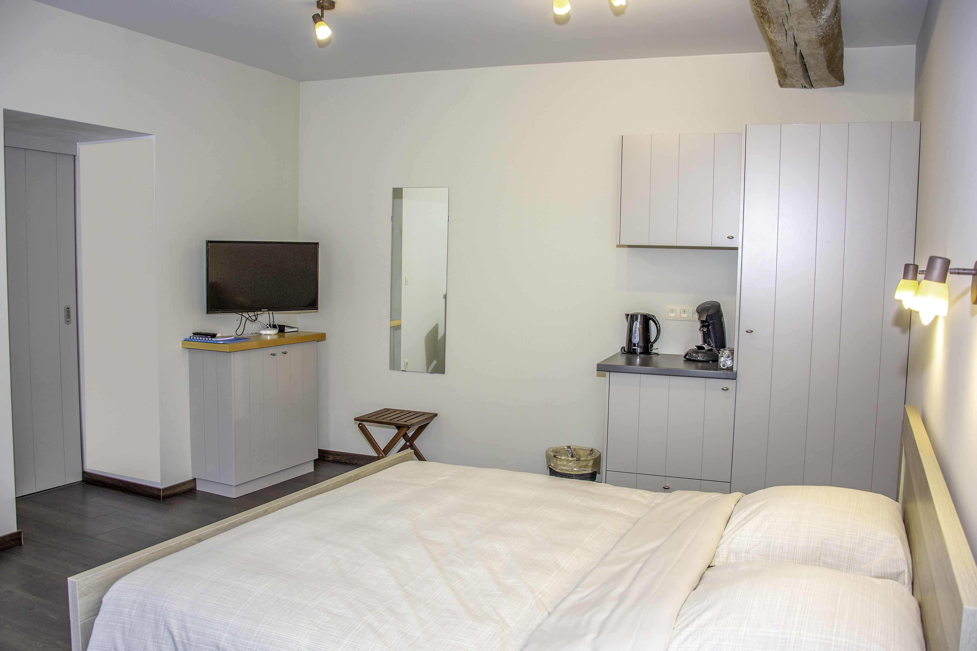 A bedroom with a bed, a television, a mirror, a small table, and a cabinet.