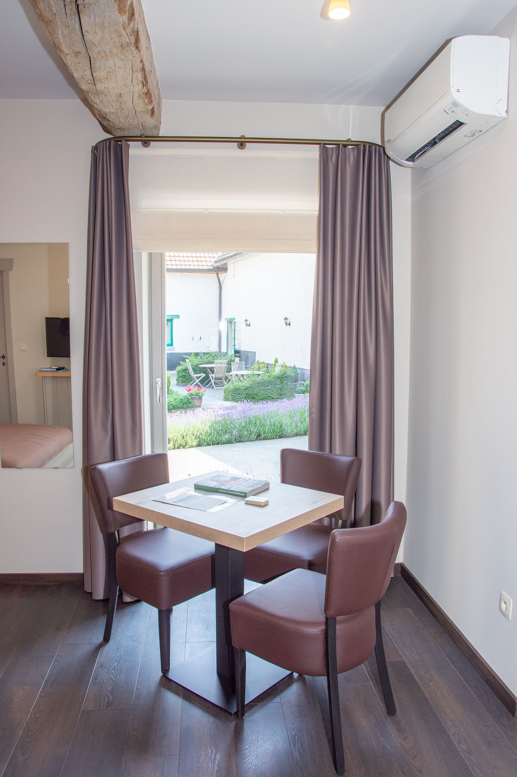Una habitación con una mesa, sillas, aire acondicionado y vistas a un jardín.