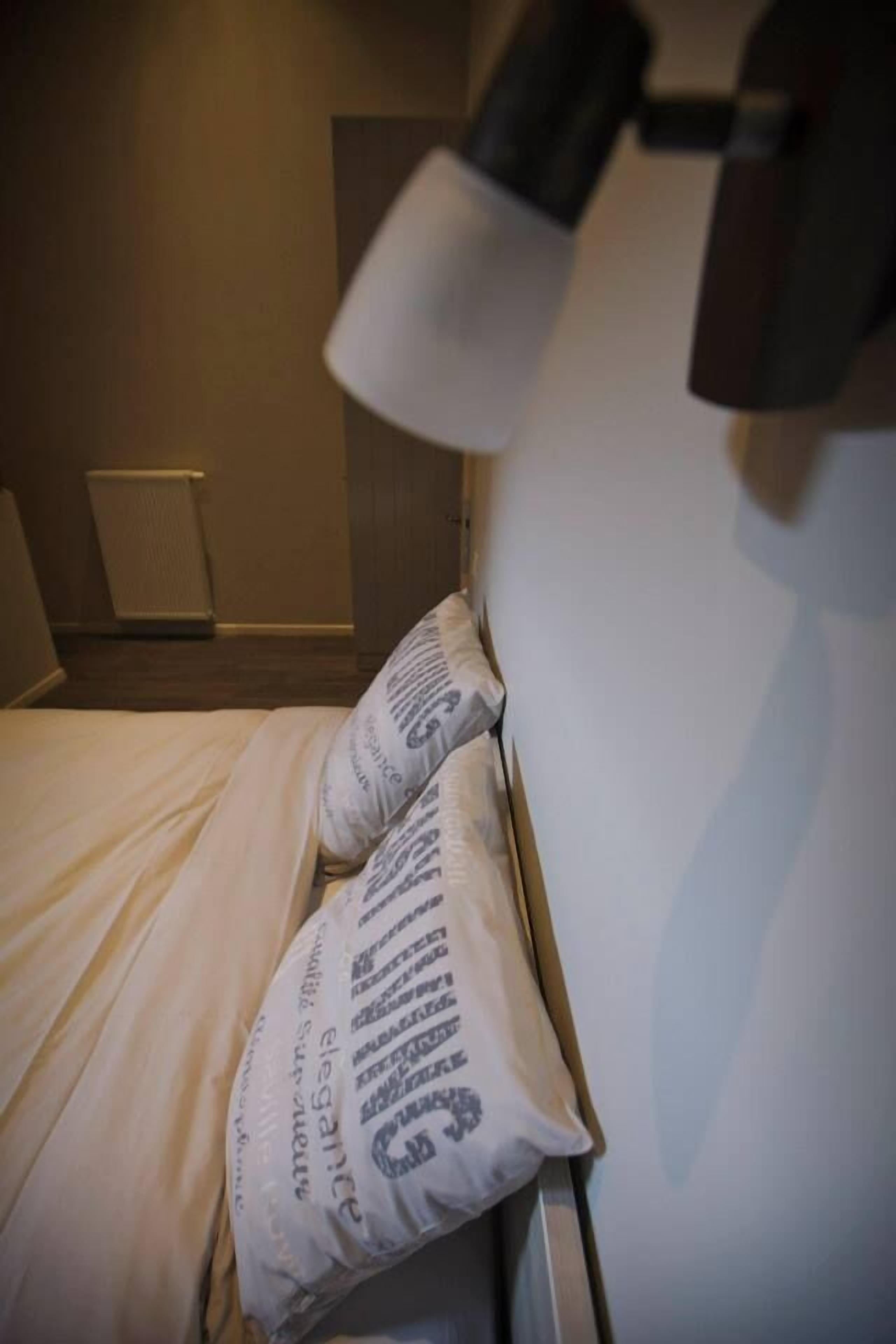 Een bed met witte beddengoed en kussens, een bedlamp en een radiator op de achtergrond.