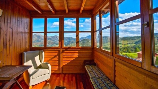 A wooden cabin with large windows, a sofa, a bench, and a rug. - El Rexacu (Onis)