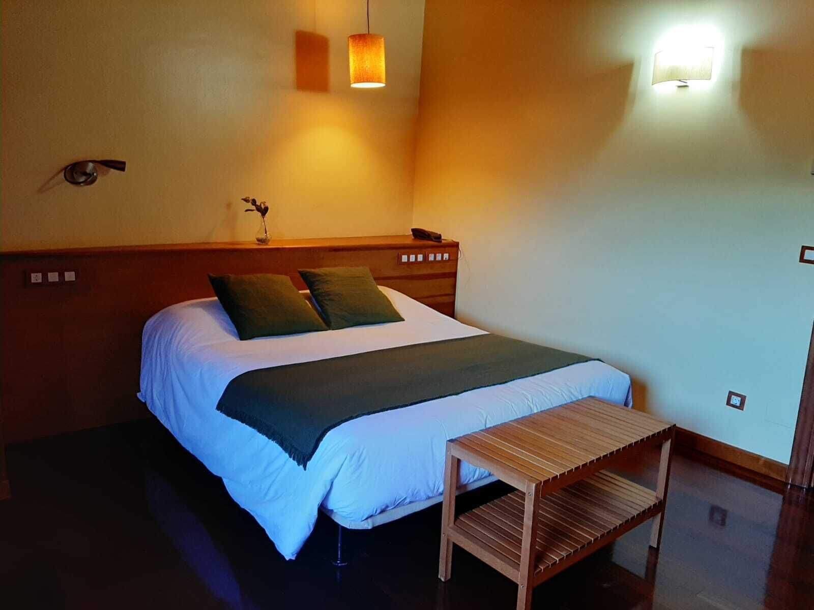 A neatly made bed with a headboard, a bedside table, and two wall-mounted lamps providing light.