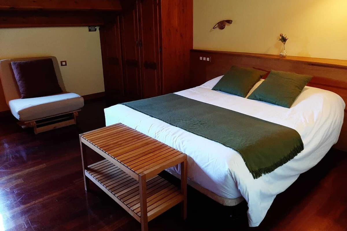 A bedroom with a bed, a bench, a chair, wooden walls, and a small wall-mounted bird sculpture.