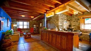 A rustic interior with a stone wall, wooden ceiling beams, a bar area, and a seating area with a sofa and chairs. - El Rexacu (Onis)