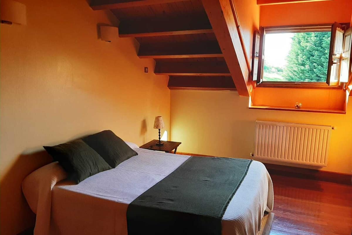 A bedroom with a bed, a nightstand, a lamp, a window, and a radiator.
